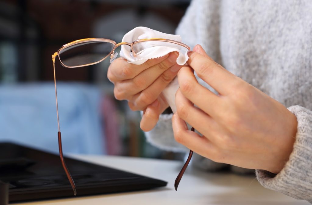 A person wearing a sweater and cleaning glasses with a soft white cloth
