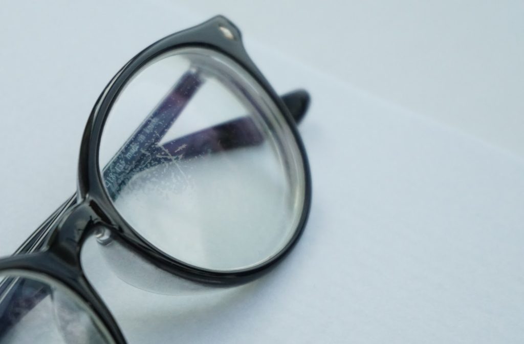 Black pair of glasses on white background with scratched lenses